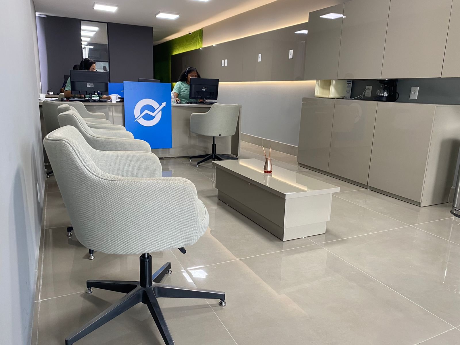 Espaço de convivência e apoio com mesa central, cadeiras escuras e revestimento de tijolo.